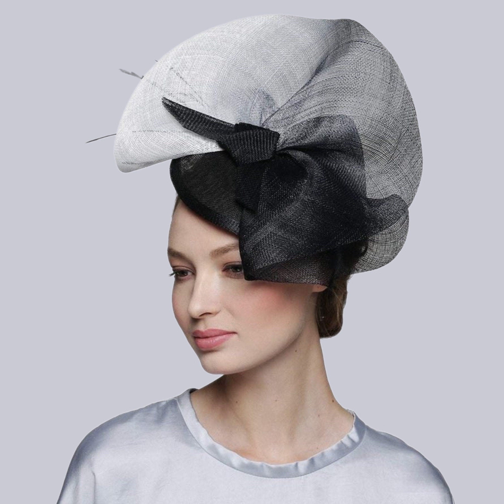A black and white fascinator hat with a large black bow. The hat is made of a delicate material.
