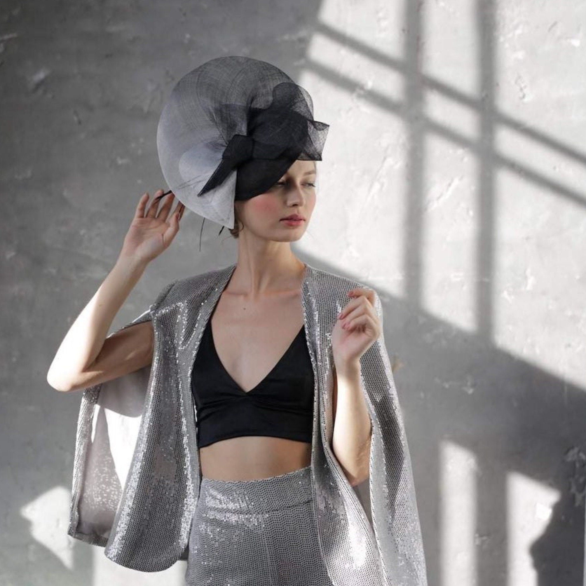 A black and white fascinator hat with a large black bow. The hat is made of a delicate material.