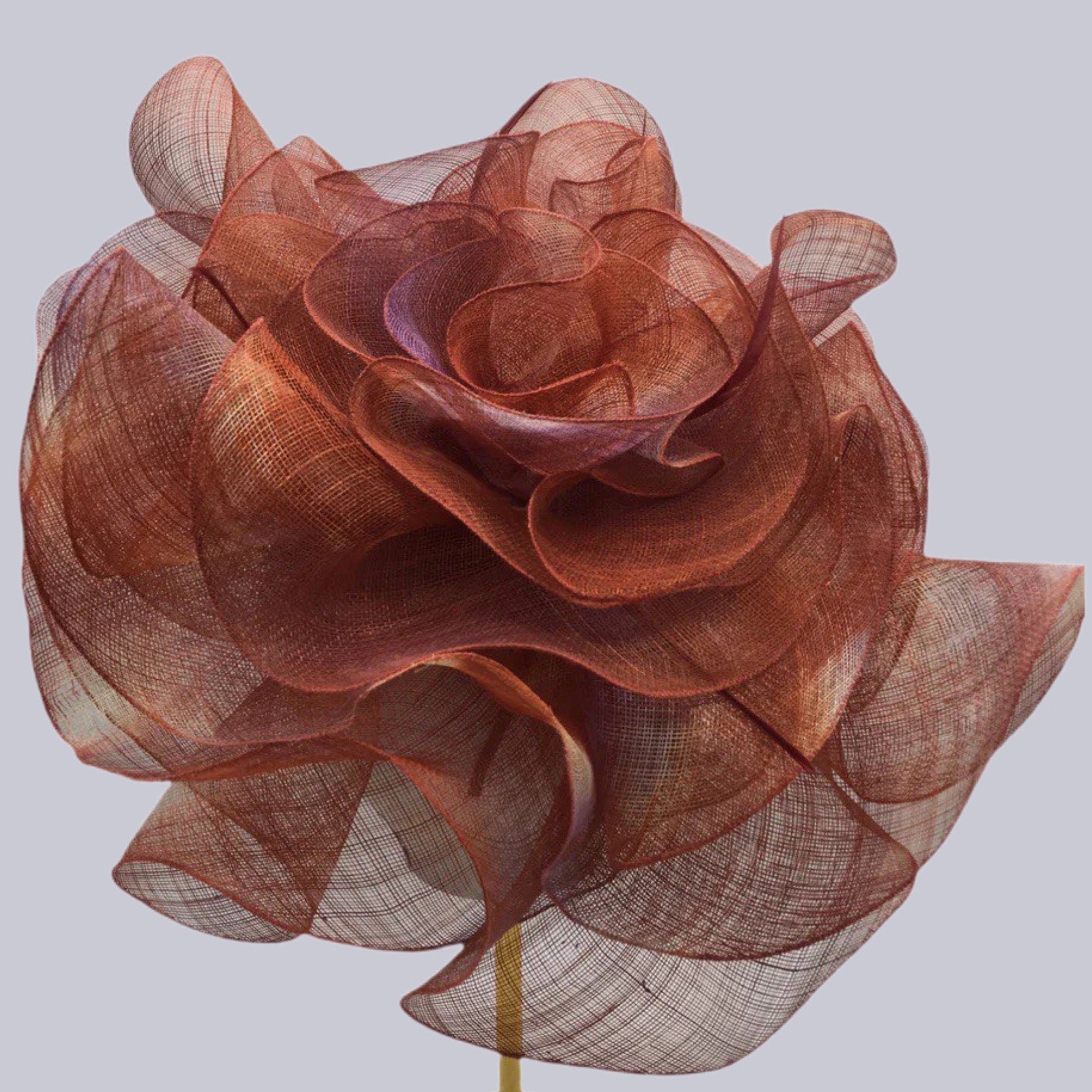 Decorative flower fascinator hat made of layered, sheer, reddish-brown fabric. The petals are ruffled and create a voluminous, textured appearance.