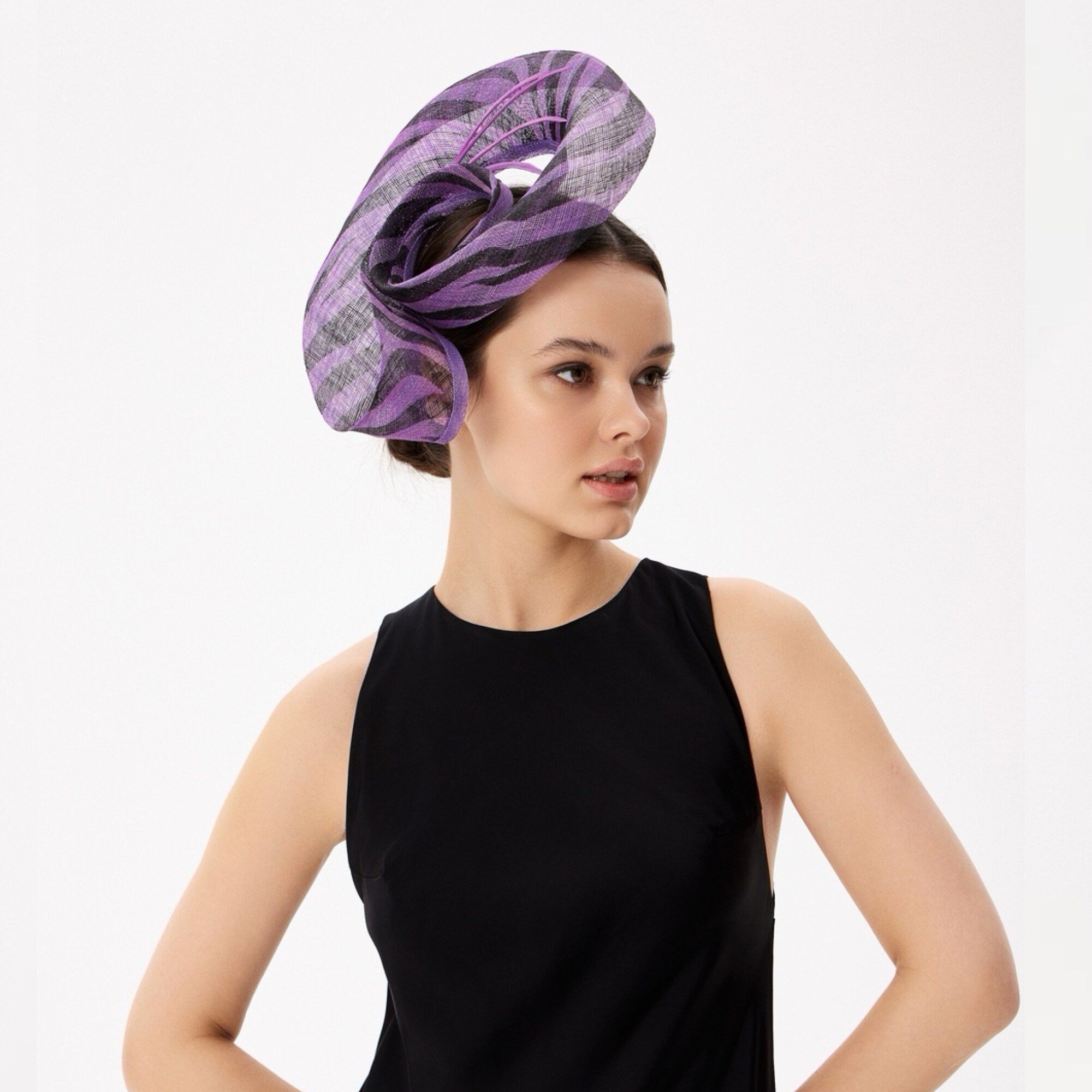 Purple and black striped headpiece, worn on the head. The headpiece is made of a sinamay and has a curved, sculptural design.