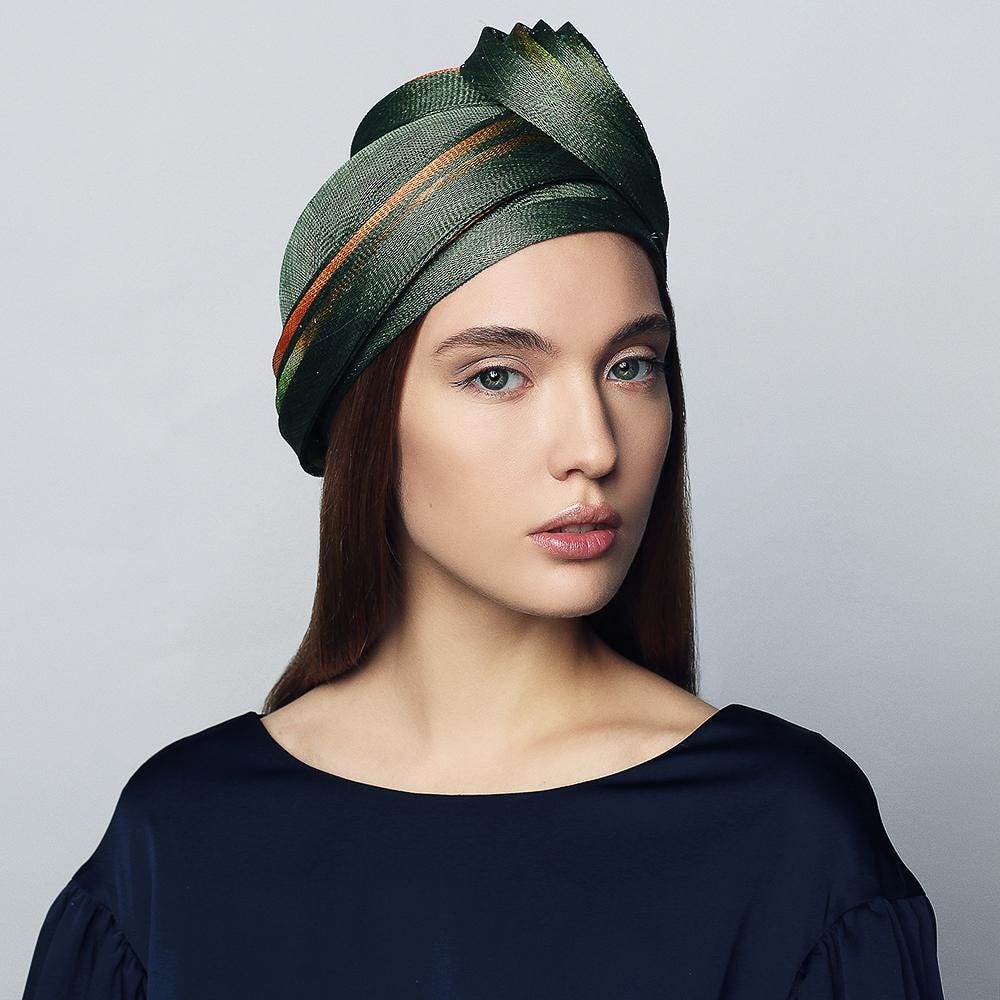Green and orange turban-style head wrap. The wrap has a pleated design and is made of a silky fabric.