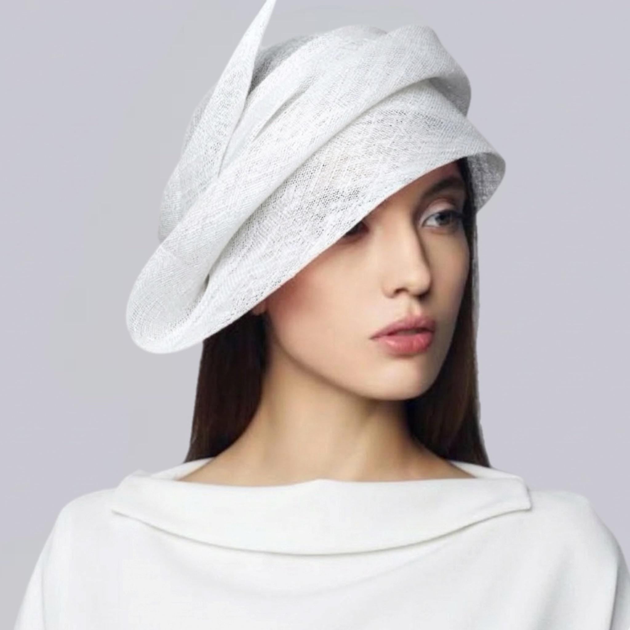 Elegant woman wearing a sculptural white sinamay straw couture hat with a sweeping wide brim for wedding guest style.
